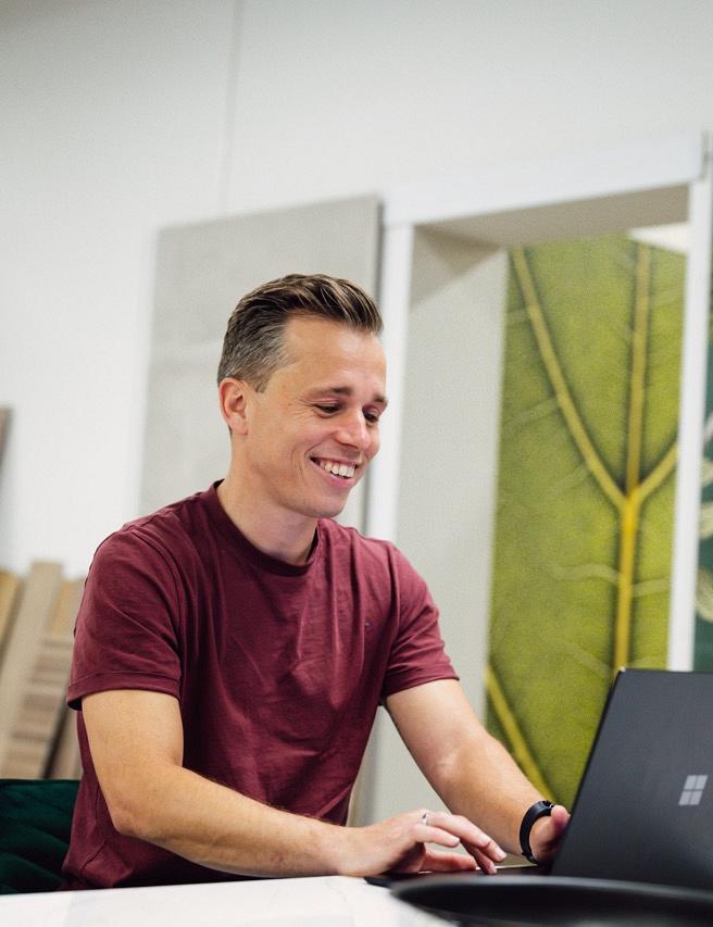 Man zit achter bureau met laptop voor zich waarop hij kijkt al glimlachend in een winkelomgeving.