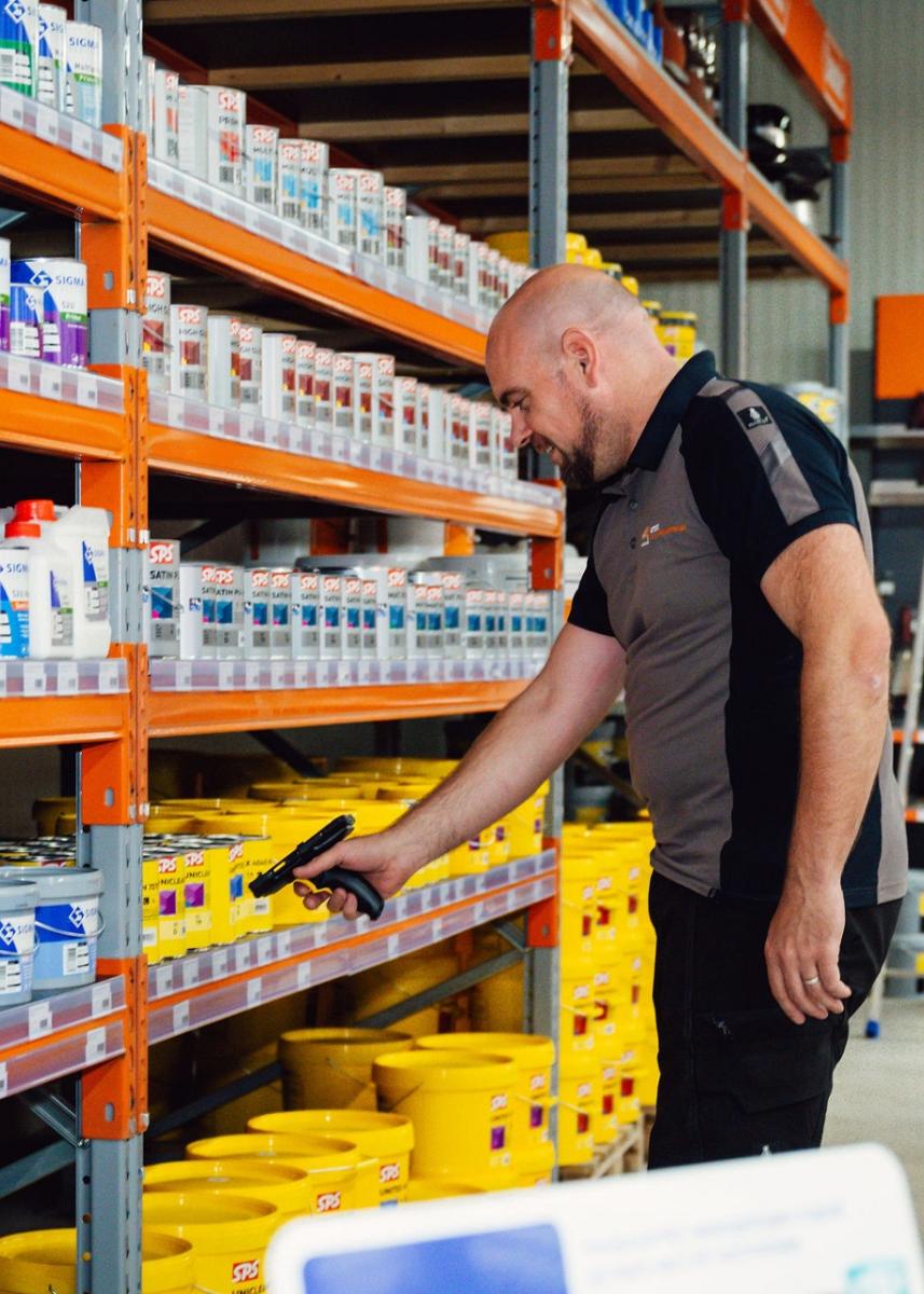 Man scant een product in een schap met verschillende verfblikken en emmers.