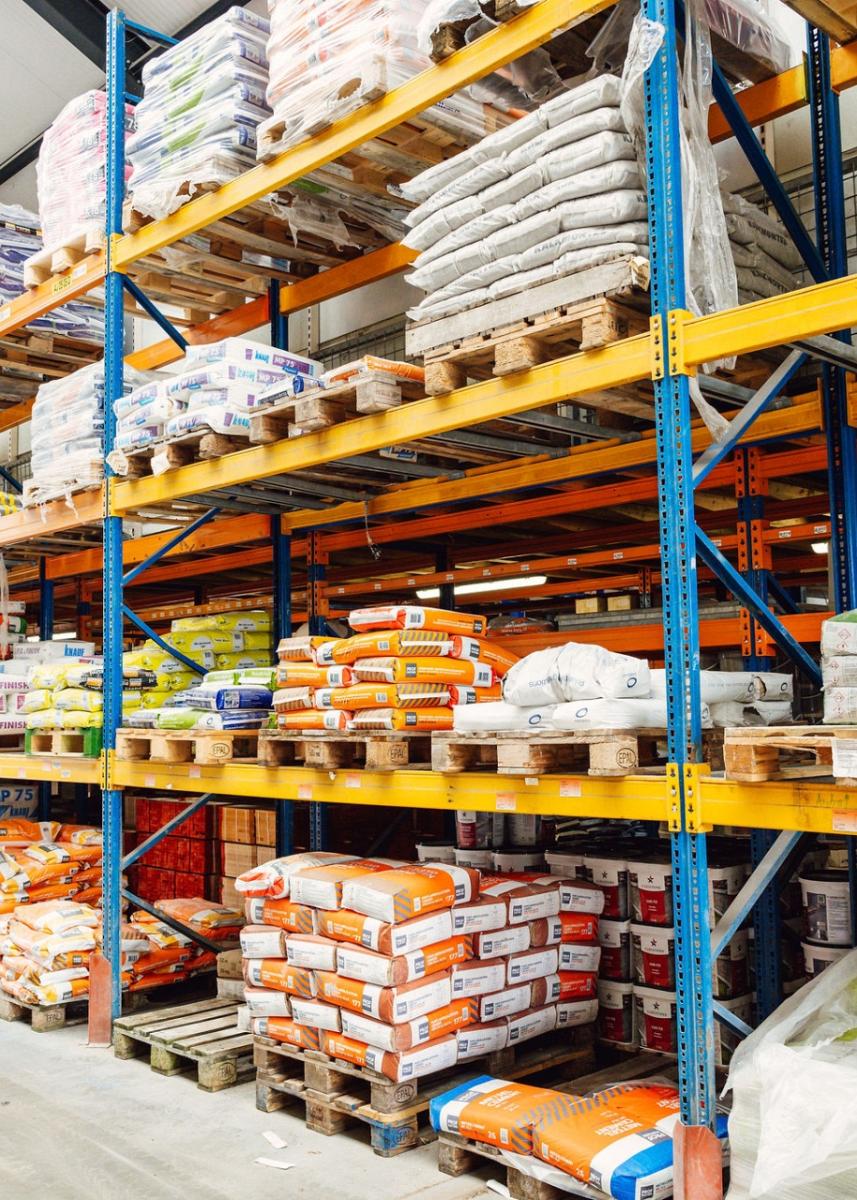 Opslagruimte met hoge stellingen gevuld met bouwmaterialen zoals cementzakken, isolatiemateriaal en verpakte producten, georganiseerd op pallets.