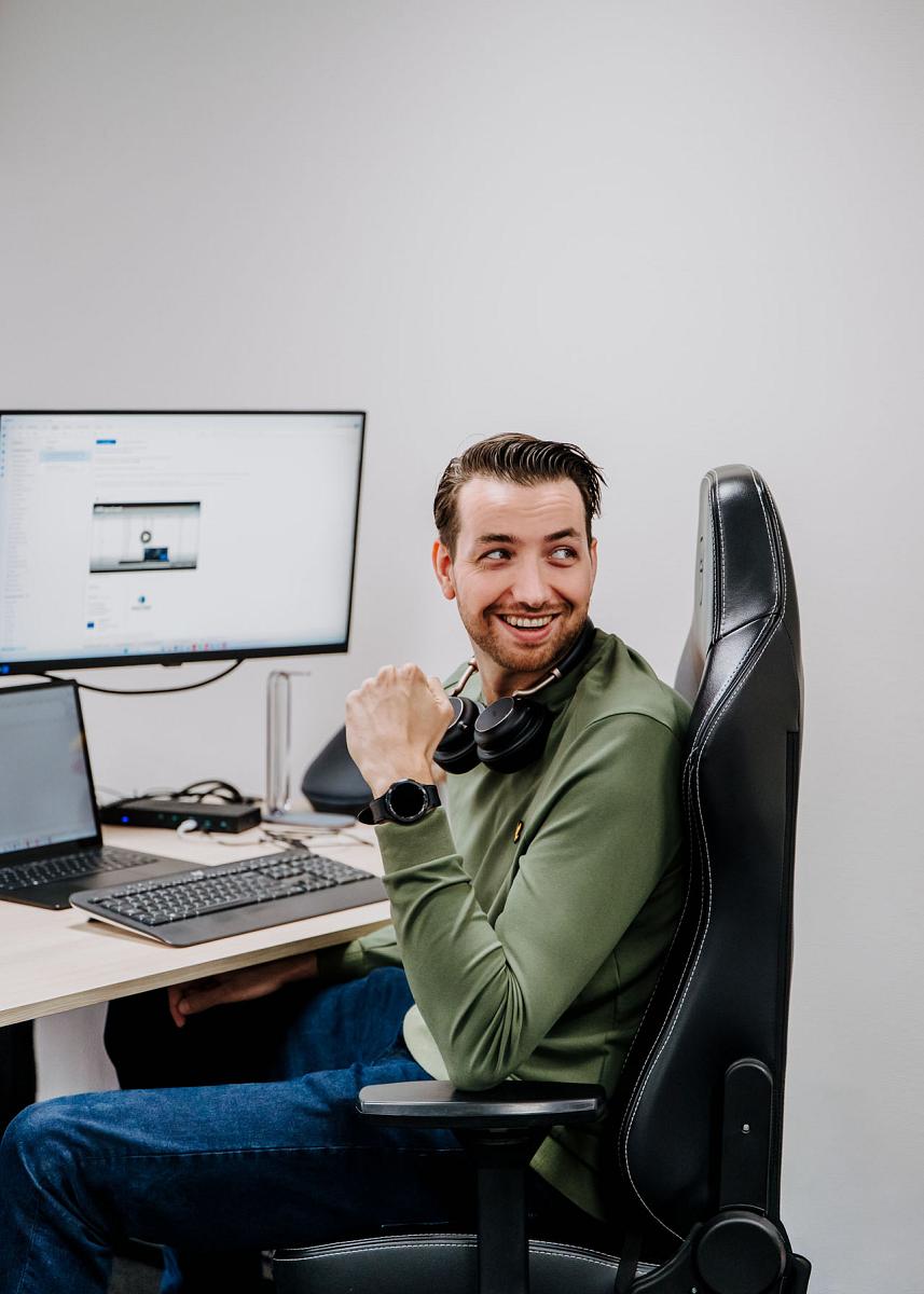 Man zit lachend achter zijn bureau met headset om zijn nek, werkend aan een computer met Smart Trade-software op het scherm.