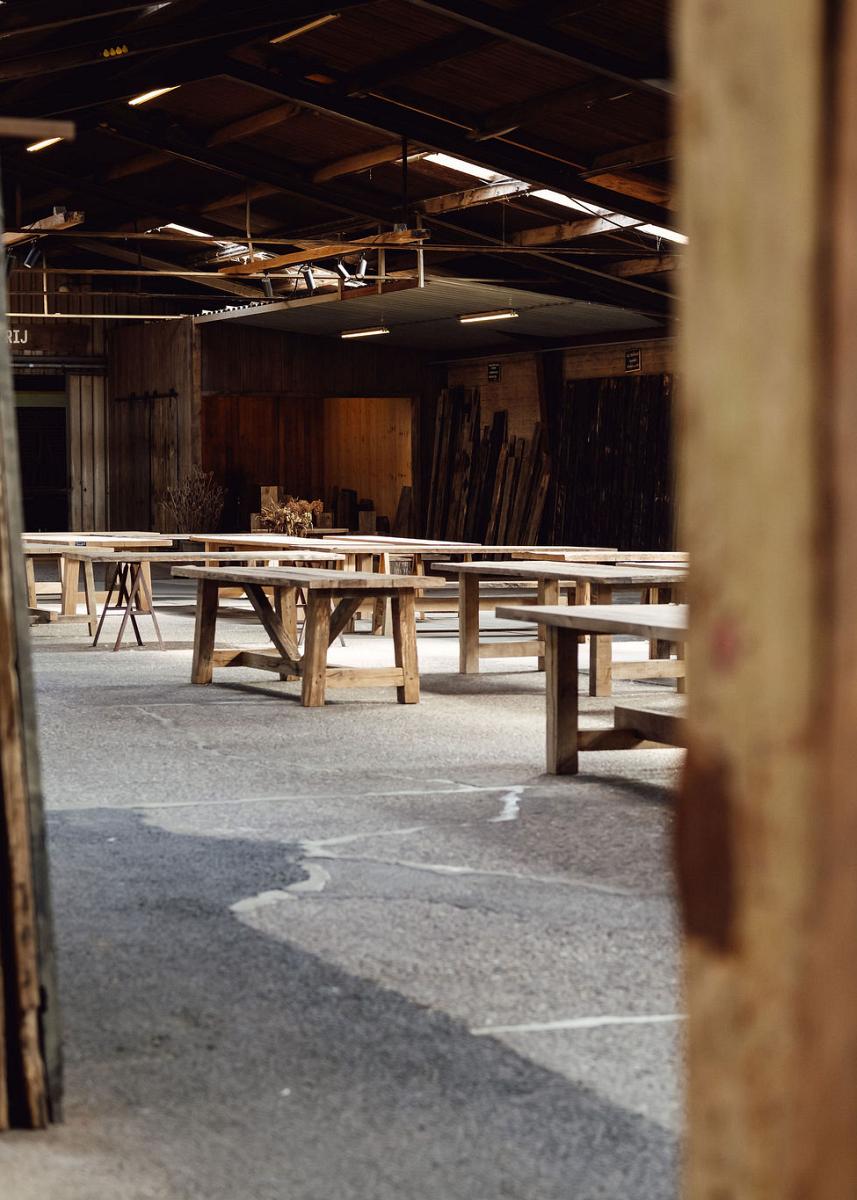 Binnenruimte van een houtloods met houten werkbanken en omringende planken, klaar voor ambachtelijk werk of workshops.