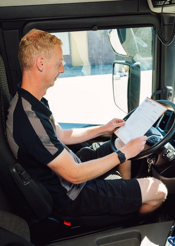  Man die achter het stuur zit van een vrachtwagen met een formulier in zijn handen waar hij naar kijkt.