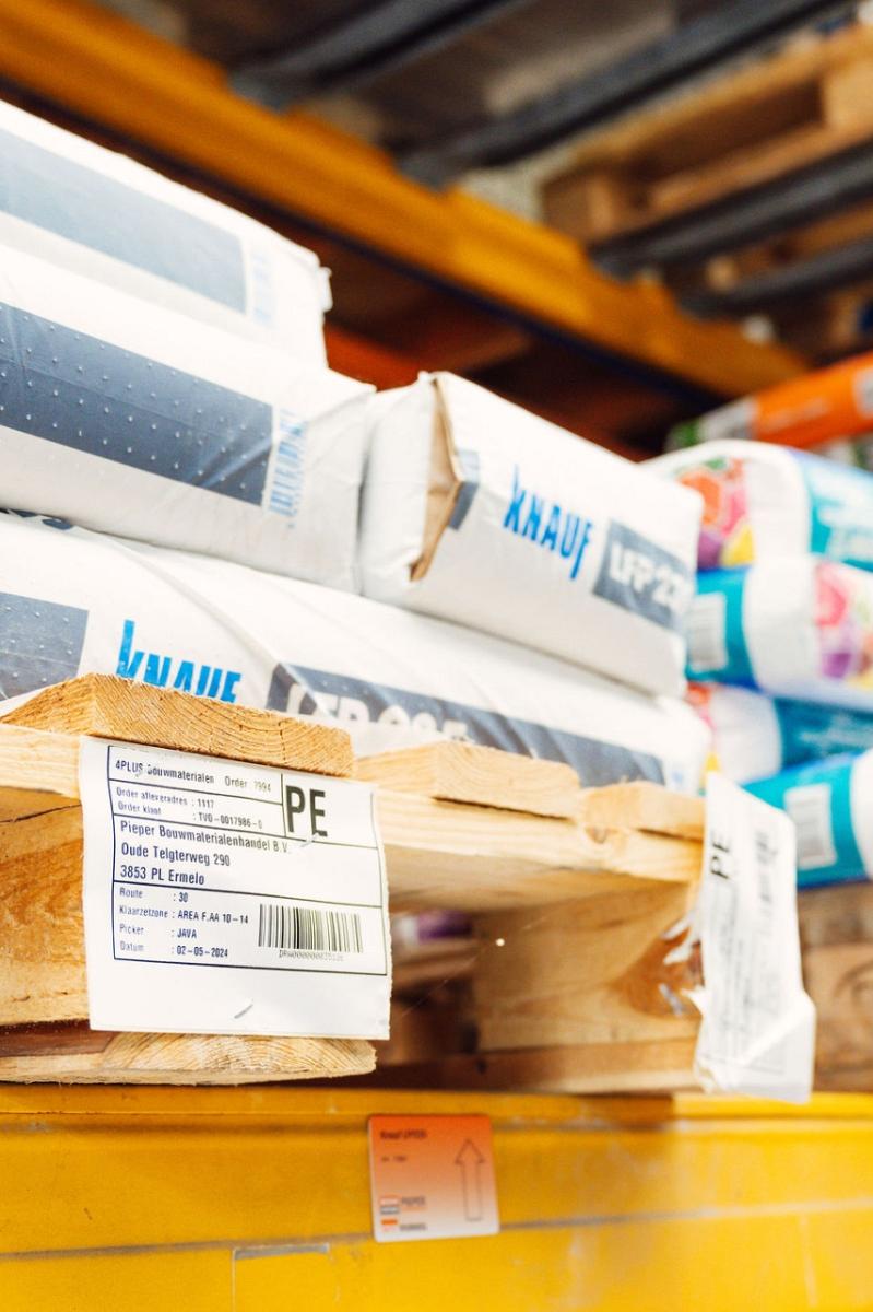 Close-up van houten pallets met daarop gestapelde bouwmaterialen, waaronder verpakkingen van Knauf LFP 235, voorzien van labels met productinformatie.
