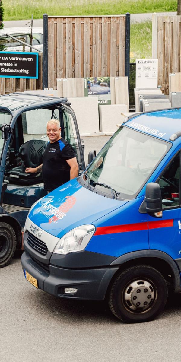 Een blauwe bestelwagen van Kippersluis Materialen met logo, naast een vorkheftruck bij een opslagplaats.