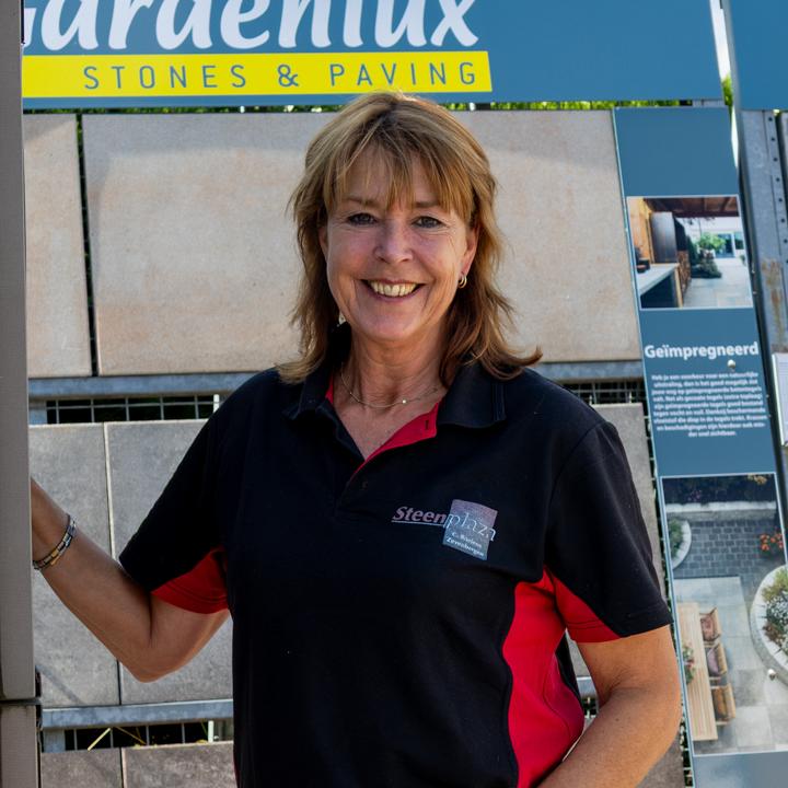 Glimlachende vrouw in een Steenplaza-polo voor een rek met tuintegels van Gardenlux.