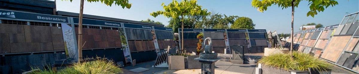 Showtuin van De Klinker Sierbestrating, met aan de linker kant een zwart tuinhuisje met overkapping, in het midden een ophoging met gras en daar omheen verschillende soorten stenen.