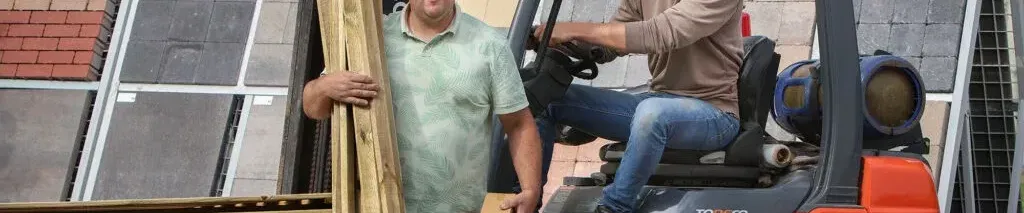 Een man die in een heftruck zit, de andere staat ervoor met hout in zijn handen.