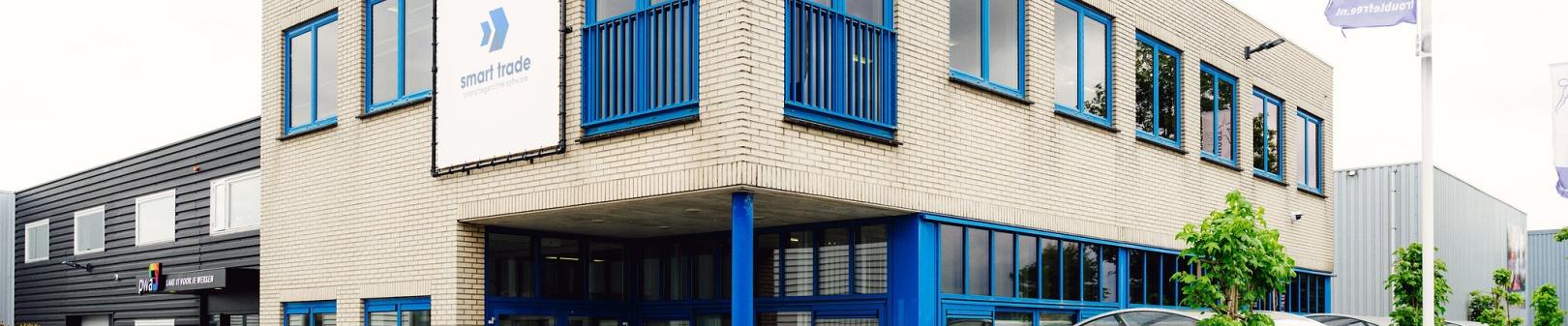 Kantoorpand van Smart Trade met licht bakstenen gevel, blauwe kozijnen en bedrijfslogo aan de voorzijde, gelegen op een bedrijventerrein.