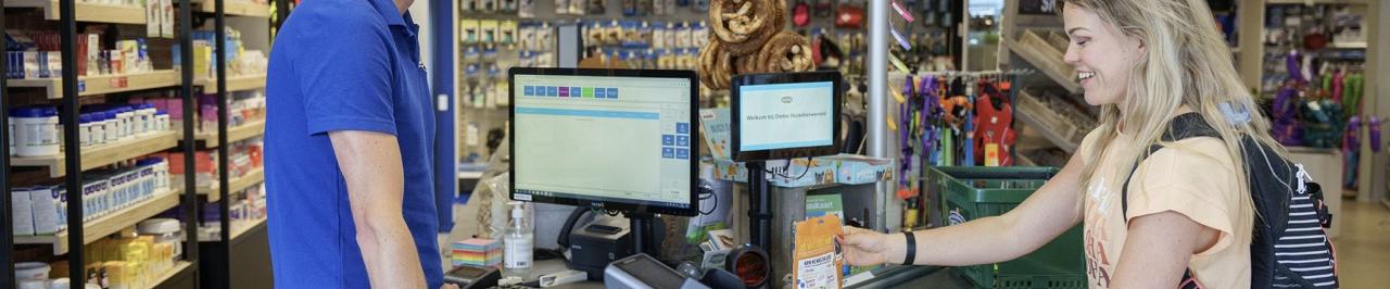 Klant rekent producten af bij de kassa van een dierenspeciaalzaak met kassasysteem en betaalterminal.