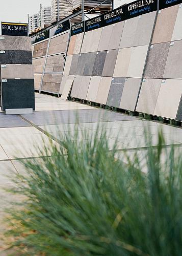 Een buitenomgeving met een selectie buitentegels op schuinstaande displays met plant op de voorgrond.