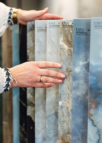 Vrouw bekijkt een reeks luxe tegelstalen van het merk EMIL met marmer- en natuursteenlook, en voelt met haar hand aan de textuur van de oppervlakken.