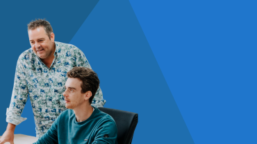 Twee medewerkers van Smart Trade bij een computer, met een blauwe achtergrond.