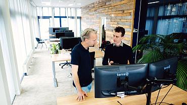Twee mannen overleggen en staan achter bureau met monitor