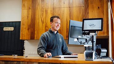 Man achter balie werkt met kassasysteem en computer in showroom van bouwmaterialenhandel.