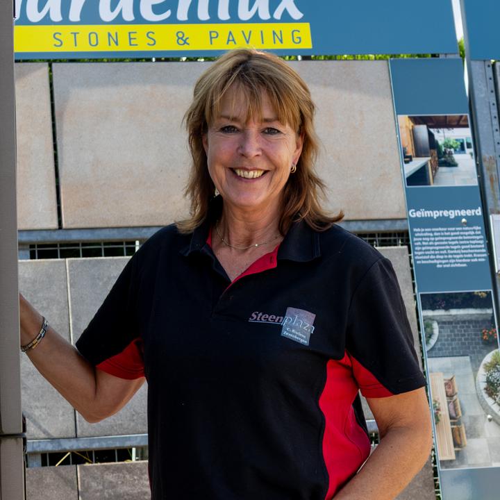 Glimlachende vrouw in een Steenplaza-polo voor een rek met tuintegels van Gardenlux.