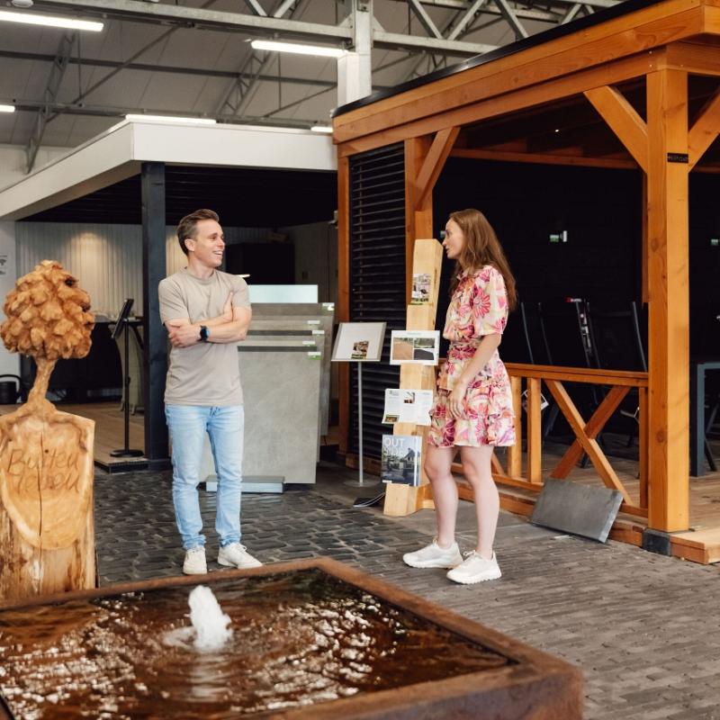 Medewerkers van Nieuwenhuis Buitenleven in gesprek in de showroom met tuinmaterialen en overkappingen.